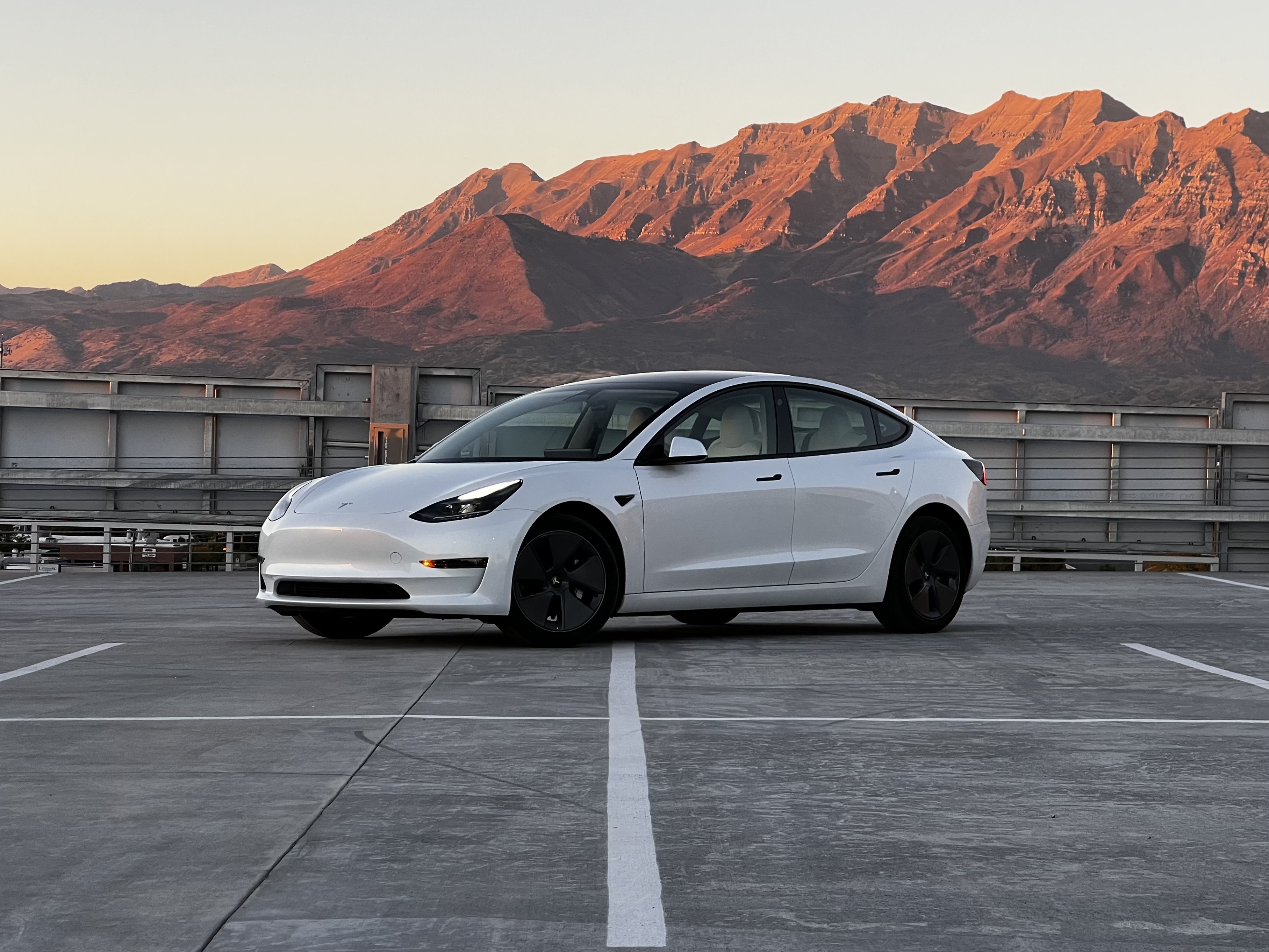 White Tesla Model 3 parked with mountains at sunset